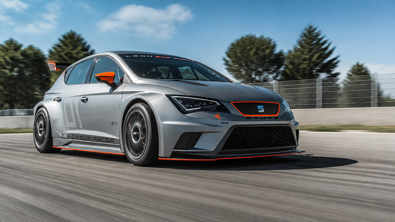 Carro de corrida Seat Leon Cup Racer cinzento com detalhes laranja em pista de corrida sob céu azul.