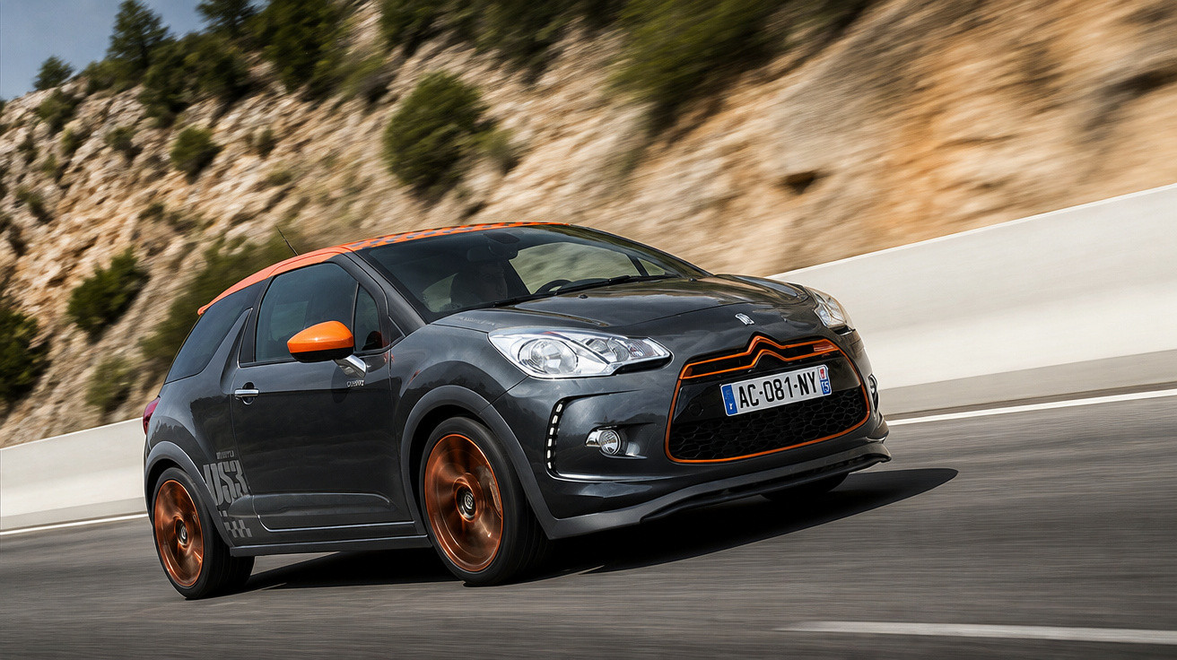 Carro Citroën DS3 cinza com detalhes laranja a alta velocidade numa estrada junto a desfiladeiro rochoso.